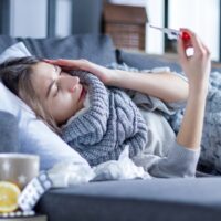 Sick girl in scarf lying in bed wrapped in blanket.