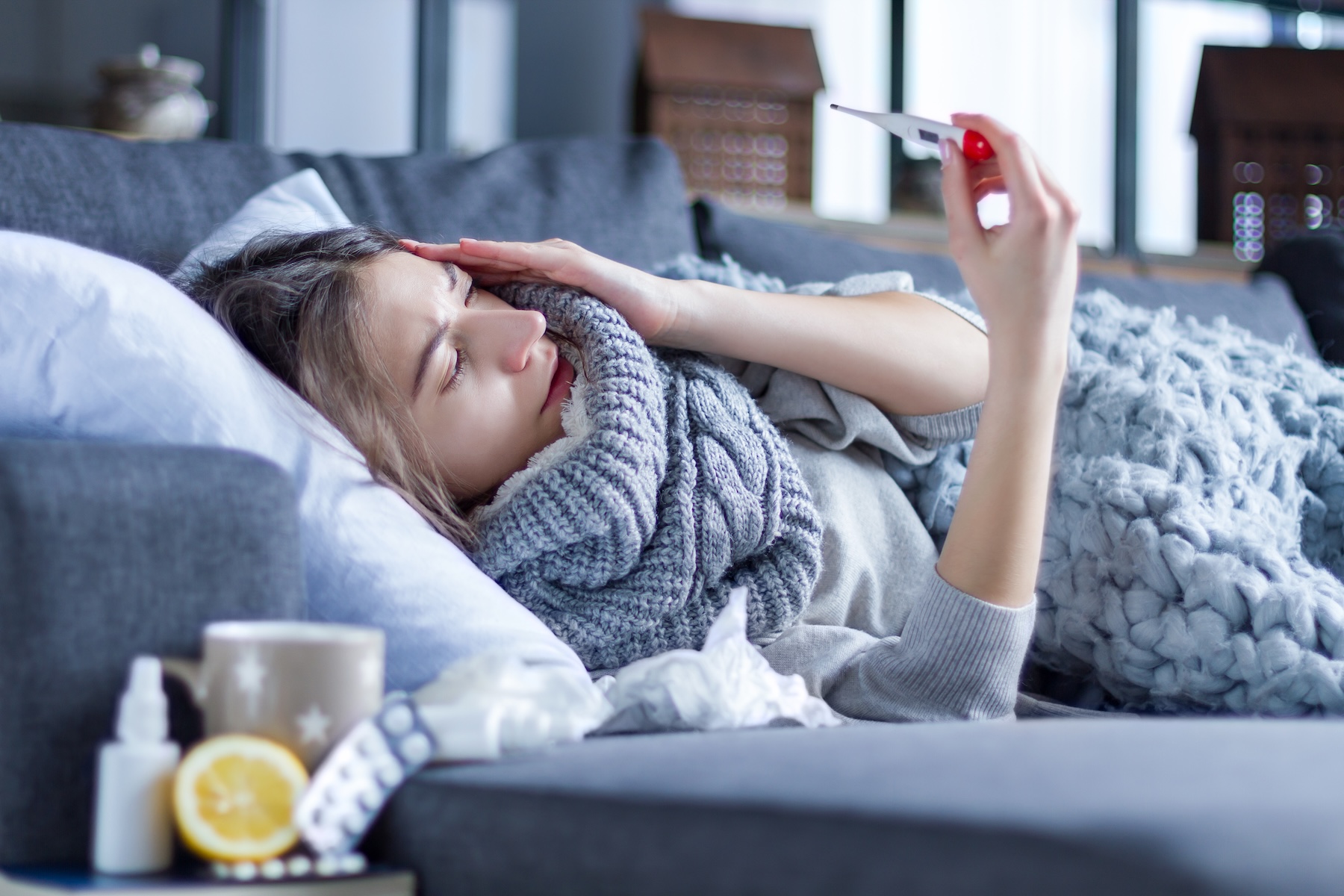 Sick girl in scarf lying in bed wrapped in blanket.