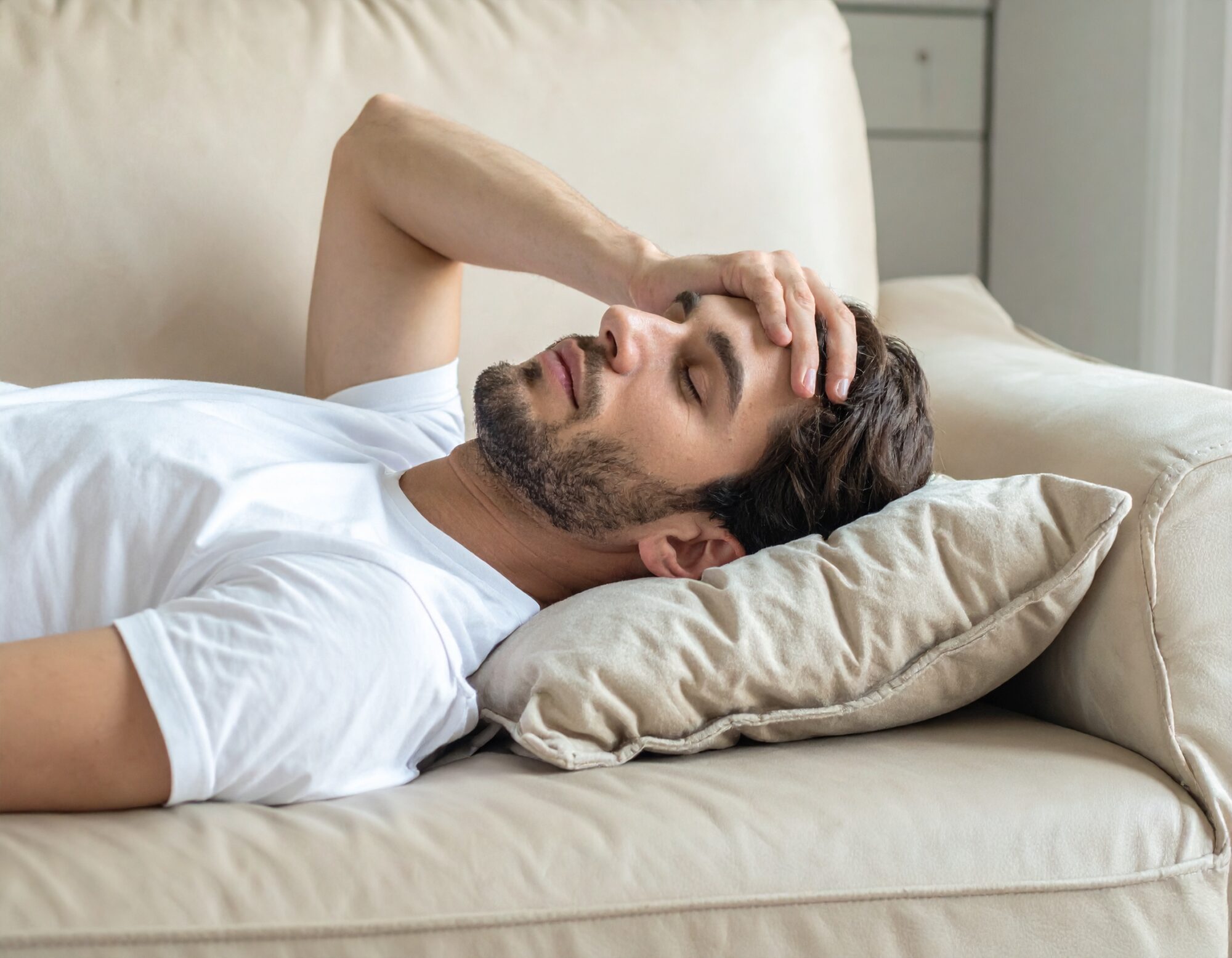 A man lies on a sofa with a migraine.