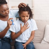 Mother giving blue asthma inhaler to her sick breathless child at home
