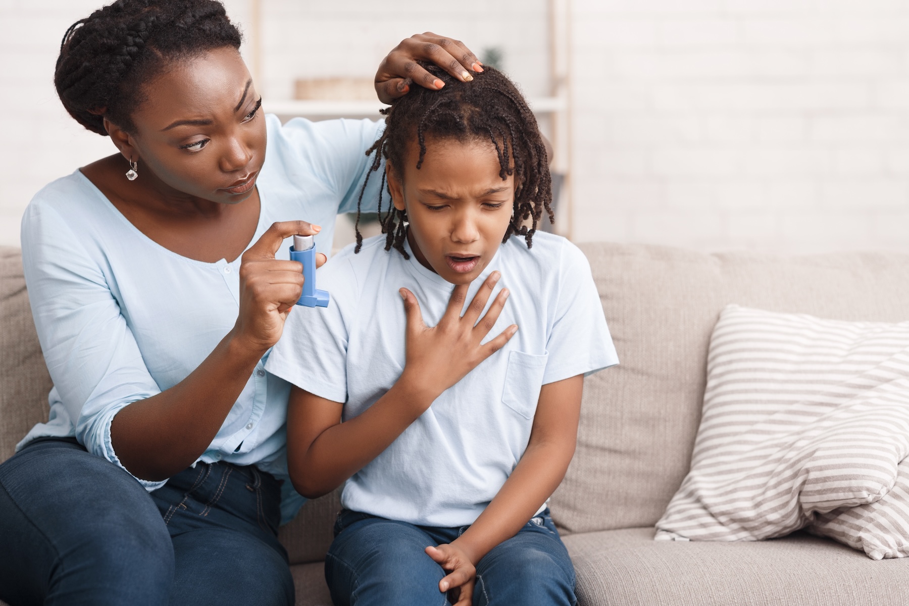 Mother giving blue asthma inhaler to her sick breathless child at home