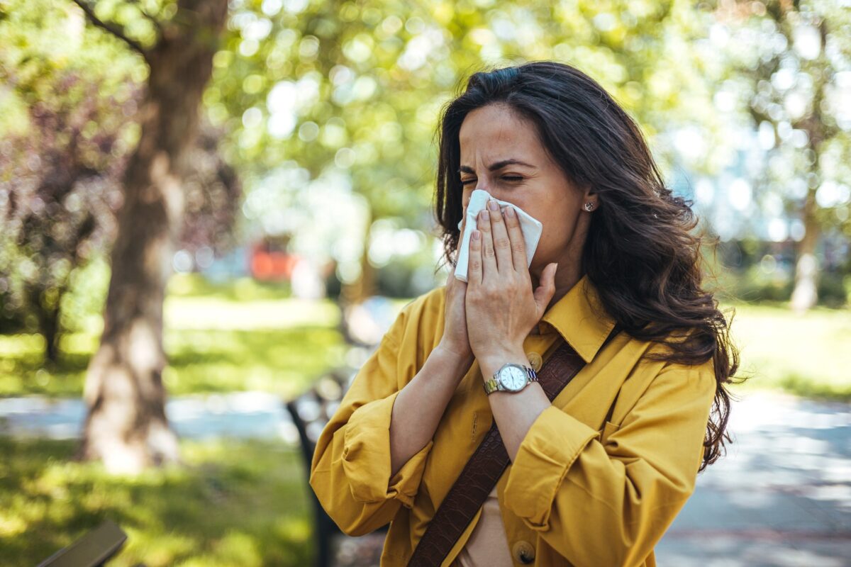 Woman in yellow top blowing nose in the park because of allergies