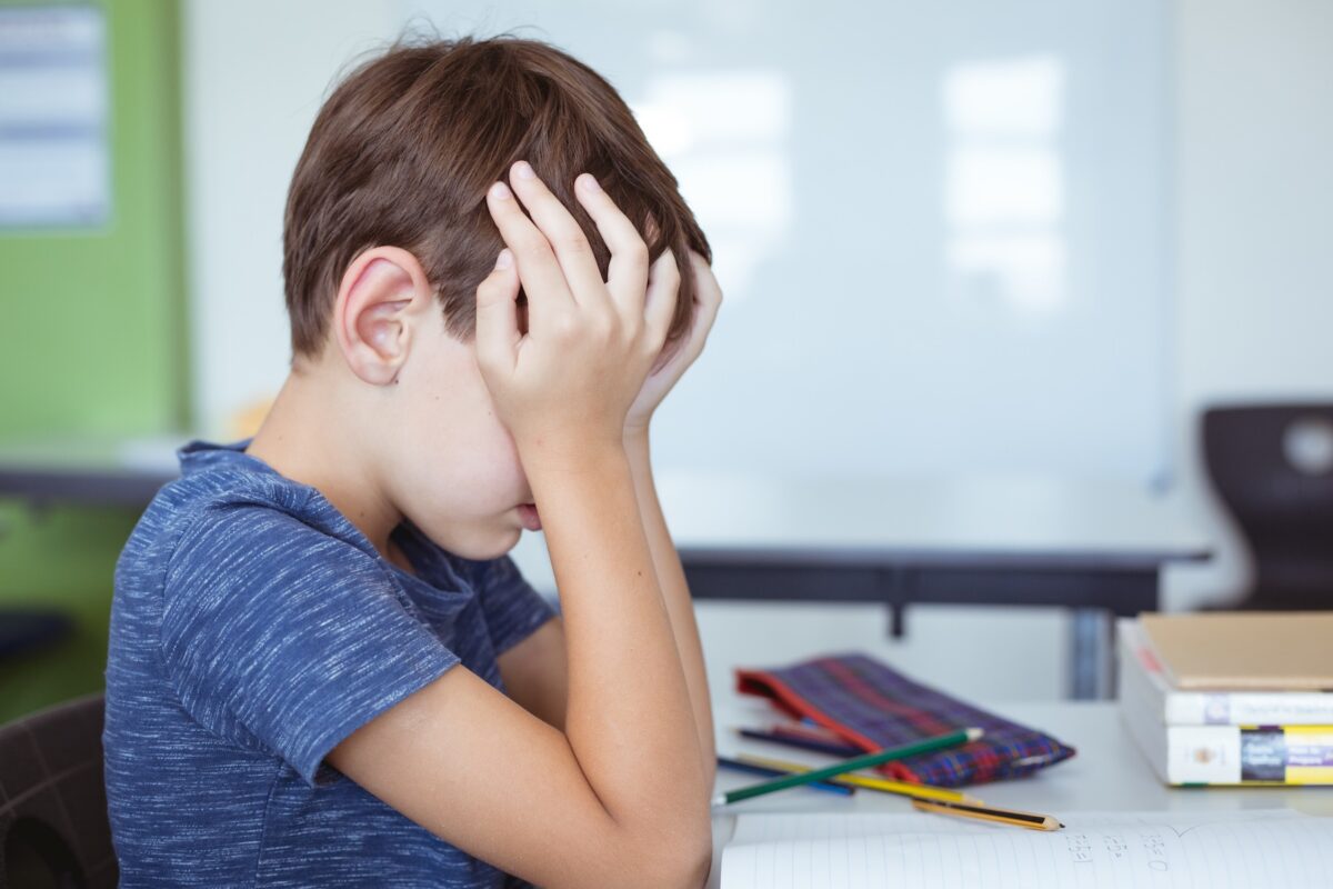 Young boy sitting in school, rubbing eyes with the palms of his hands