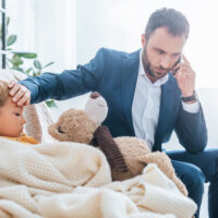 Father calling docor while holding hand to son's forehead, checking for fever