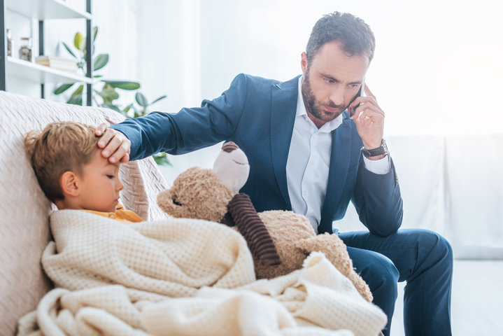 Father calling docor while holding hand to son's forehead, checking for fever